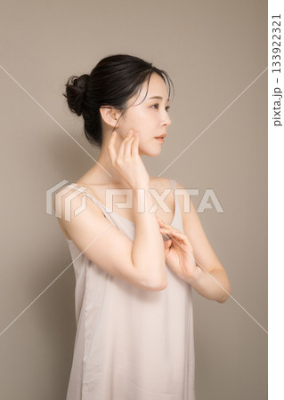髪の毛がアップ背景がベージュの使いやすい美容やスキンケアの美しい女性のイメージ上半身　手で頬を触る 133922321