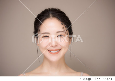 髪の毛がアップ背景がベージュの使いやすい美容やスキンケアの美しい女性のイメージ　カメラ目線正面　 133922324