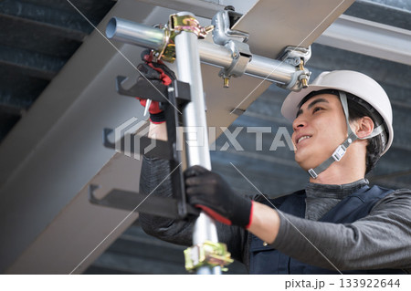 天井が近い高所の足場で単管パイプを固定するクランプなどの施工作業 鳶職や作業員のイメージ レンチ 天井が近い高所の足場で単管パイプを固定するクランプなどの施工作業 鳶職や作業員のイメージ レンチ 133922644