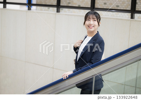 空港や駅のエスカレーターを降りるスーツ姿のキャリア女性のビジネス交通機関移動シーン　振り返る	 133922648