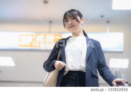 空港や駅のエスカレーターを降りるスーツ姿のキャリア女性のビジネス移動シーン　カメラ目線	 133922650