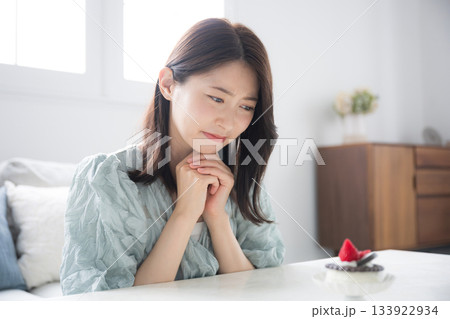 甘いスイーツを食べるか迷う女性　スイーツは別腹だけどダイエットで悩む	 133922934