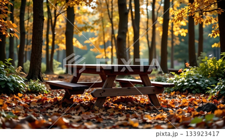 A serene autumnal park setting. In the center of the frame is a wooden picnic table, flanked by benches A serene autumnal park setting. In the center of the frame is a wooden picnic table, flanked by benches 133923417