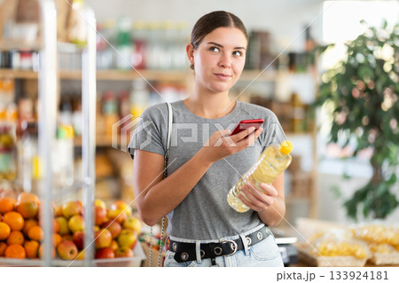 In shop youth girl scan QR code and take reading vegetable oil package bottle using phone camera In shop youth girl scan QR code and take reading vegetable oil package bottle using phone camera 133924181