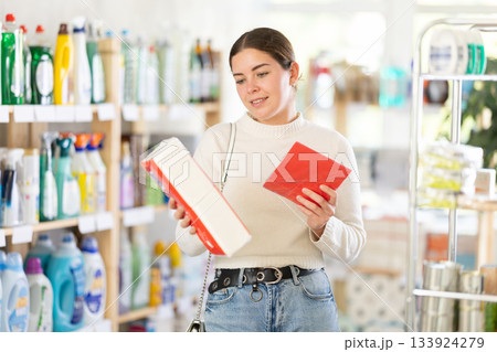 Young woman housewife in household store examines package, chooses paper napkin 133924279