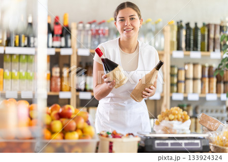 Young woman seller offering wine in grocery store Young woman seller offering wine in grocery store 133924324