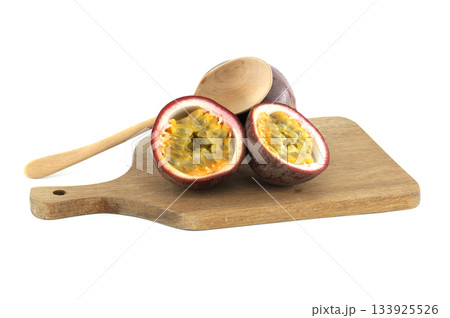 Fresh passion fruits cut in half showing the pulp and seeds, lying on wooden cutting board with wooden spoon 133925526