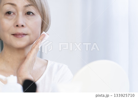 明るい窓際でメイクをするシニア女性 明るい窓際でメイクをするシニア女性 133925710