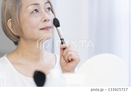 明るい窓際でメイクをするシニア女性 133925727