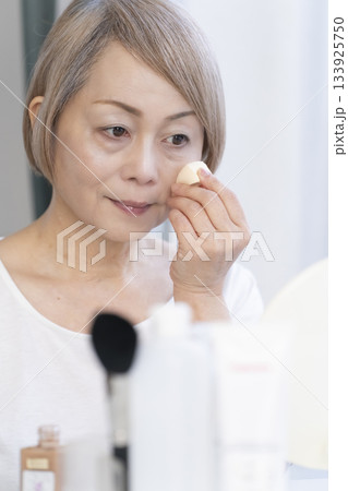 明るい窓際でメイクをするシニア女性 133925750
