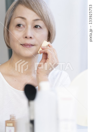 明るい窓際でメイクをするシニア女性 明るい窓際でメイクをするシニア女性 133925753