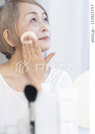 明るい窓際でメイクをするシニア女性 明るい窓際でメイクをするシニア女性 133925757