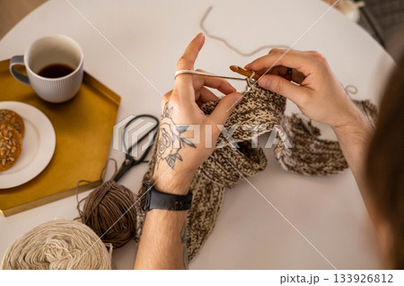 Feminine male hands crochet handmade artwork hobby wooden table with sewing tools closeup top view Feminine male hands crochet handmade artwork hobby wooden table with sewing tools closeup top view 133926812