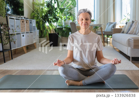 Smiling mature gray haired sport woman sits on yoga mat in lotus position. elderly lady meditates 133926838