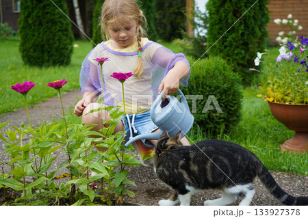 A youthful gardener radiates joy while watering her colorful flower collection with a vintage watering can during a pleasant summer gardening session. 133927378