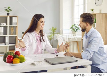 Nutritionist woman giving consultation to smiling young man patient in clinic. 133927813