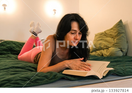 Russian 50 year old woman calmly turning a page while reading in bed enjoying a quiet mindful moment relaxation balance and gentle evening focus Russian 50 year old woman calmly turning a page while reading in bed enjoying a quiet mindful moment relaxation balance and gentle evening focus 133927814