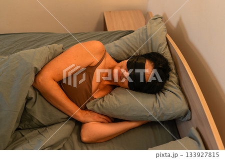 Sleeping 50 year old Russian woman rests on her side in a sleep mask, showing calmness, deep relaxation and a peaceful mindful night routine. 133927815