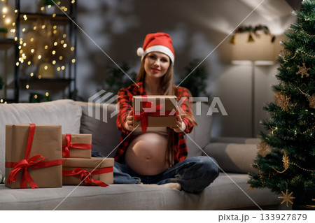 A pregnant woman wearing a Santa hat offers a wrapped gift during the Christmas season A pregnant woman wearing a Santa hat offers a wrapped gift during the Christmas season 133927879