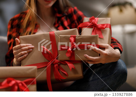 A woman in a red plaid shirt holds several wrapped gifts with red ribbons, perfect for a special occasion 133927886