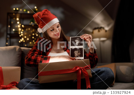 A woman in a Santa hat reveals her ultrasound during Christmas, celebrating the upcoming arrival of her baby A woman in a Santa hat reveals her ultrasound during Christmas, celebrating the upcoming arrival of her baby 133927924
