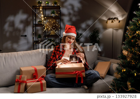 A woman in a Santa hat opens a gift box to reveal an ultrasound during the Christmas holiday season 133927928