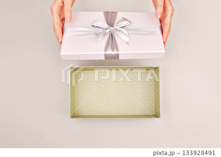 Woman opening empty gift box silver ribbon bow Cloud Dancer background Woman opening empty gift box silver ribbon bow Cloud Dancer background 133928491