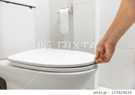 Close up hand is opening the lid of a toilet seat. 133929016