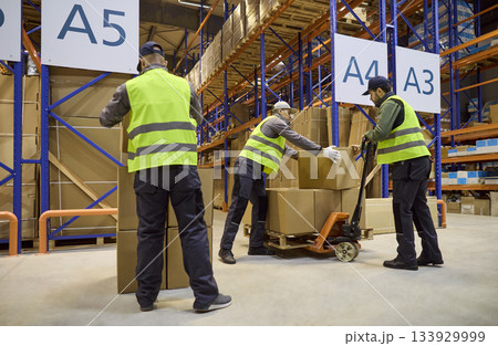 Warehouse workers loading boxes onto pallet jack for efficient order dispatch Warehouse workers loading boxes onto pallet jack for efficient order dispatch 133929999
