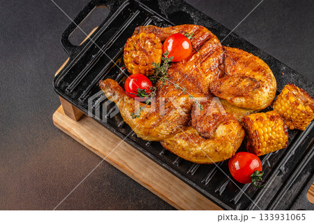 Grilled golden chicken with corn and cherry tomatoes served on a cast-iron grill skillet, top view 133931065