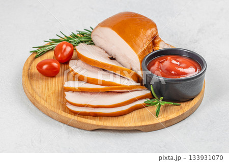 Sliced smoked chicken breast served on a wooden board with cherry tomatoes, rosemary, and ketchup on a light background 133931070