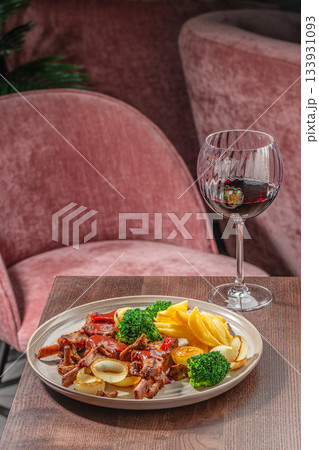 Grilled meat with roasted vegetables, broccoli and fries served on a rustic plate with a glass of red wine in a cozy restaurant setting 133931093