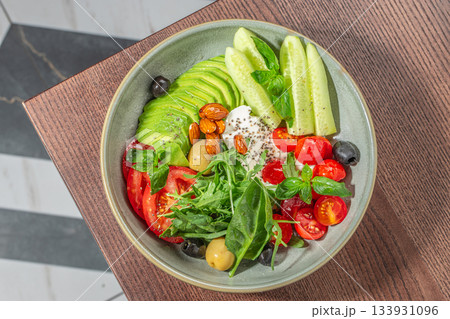 Fresh vibrant salad bowl with avocado, cucumbers, tomatoes, greens, olives, nuts and creamy cheese for a healthy colorful meal presentation 133931096
