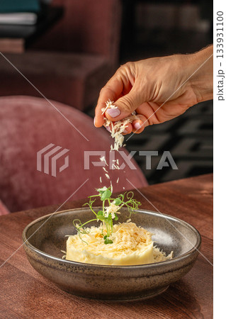 Hand sprinkling freshly grated parmesan over a gourmet plated dish with creamy puree and microgreens in a fine dining restaurant 133931100