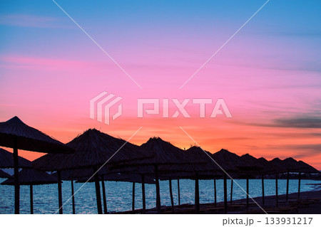 Seascape in the evening. Deserted tropical beach scenery with the silhouette of sun parasols and evening sky Seascape in the evening. Deserted tropical beach scenery with the silhouette of sun parasols and evening sky 133931217