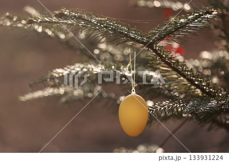 A golden egg ornament hangs from a Christmas tree 133931224