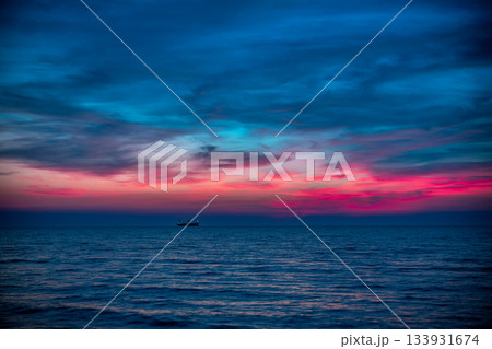 Silhouette of Cargo Ship on Calm Ocean at Dusk Under Colorful Sunset Sky Over Horizon Silhouette of Cargo Ship on Calm Ocean at Dusk Under Colorful Sunset Sky Over Horizon 133931674