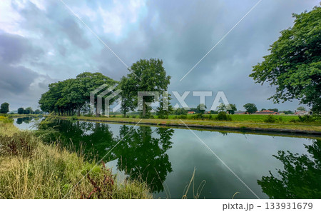 Tranquil rural landscape featuring mirrored water beneath dark clouds Tranquil rural landscape featuring mirrored water beneath dark clouds 133931679
