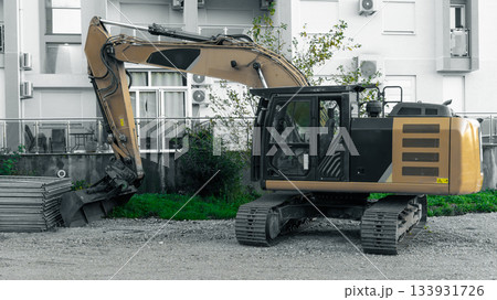 Yellow Excavator at Urban Construction Site With Buckets and Tracks in Front of Apartment Buildings Yellow Excavator at Urban Construction Site With Buckets and Tracks in Front of Apartment Buildings 133931726