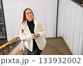 A Caucasian woman thoughtfully walks up the stairs with a phone in her hands. no makeup look or natural beauty. doctor, mother of two children, professor, businesswoman with long red hair 133932002