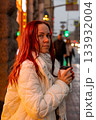 middle aged Caucasian woman drinks coffee in rain under neon lights. woman is walking alone in the city. 133932004