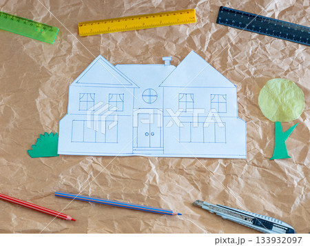 Paper house sketch with craft tools on crumpled kraft paper background, creative architectural concept 133932097