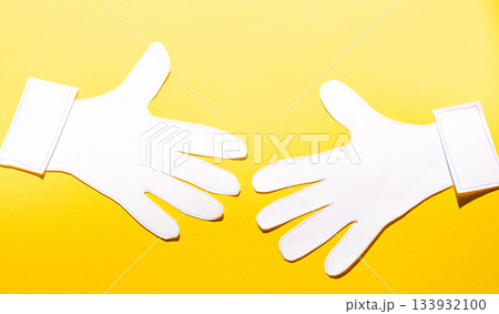 Paper cutout hands reaching toward each other on bright yellow background Paper cutout hands reaching toward each other on bright yellow background 133932100