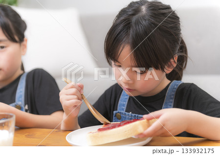 部屋で食パンにジャムを広げる子どもたちと家庭的な朝の時間 部屋で食パンにジャムを広げる子どもたちと家庭的な朝の時間 133932175