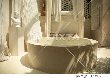 An elegant spa area featuring a round stone tub and gentle textiles An elegant spa area featuring a round stone tub and gentle textiles 133932529