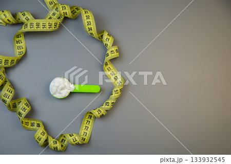 Bright yellow measuring tape forms a circle around a green scoop filled with white powder, representing health and nutrition in a clean, minimalist environment with copy space Bright yellow measuring tape forms a circle around a green scoop filled with white powder, representing health and nutrition in a clean, minimalist environment with copy space 133932545