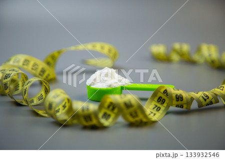 Measuring scoop with white powder is placed on a gray surface, surrounded by yellow measuring tape, representing health, fitness, and nutritional awareness in daily life 133932546