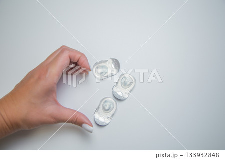 Close-up of a creative layout of disposable contact lenses in disposable protective packaging and hands that form a heart symbol on a white background. The concept of eye moisturizing, ophthalmology 133932848