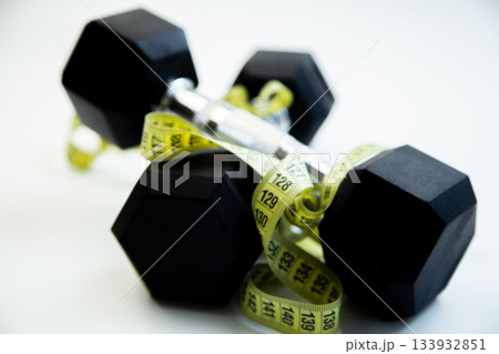 Black dumbbells are intertwined with a yellow measuring tape, representing fitness aspirations and healthy living in a clean, modern workout space Black dumbbells are intertwined with a yellow measuring tape, representing fitness aspirations and healthy living in a clean, modern workout space 133932851