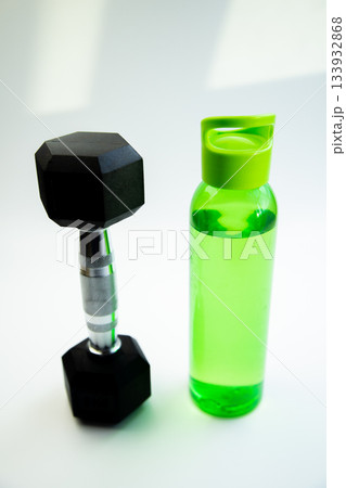Hexagonal dumbbell placed beside a vibrant green water bottle on a bright surface, representing fitness, hydration, and a commitment to a healthy lifestyle Hexagonal dumbbell placed beside a vibrant green water bottle on a bright surface, representing fitness, hydration, and a commitment to a healthy lifestyle 133932868